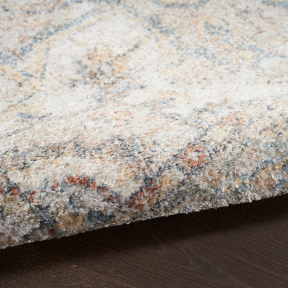 Close-up of a soft, multicolor area rug in beige, blue, and rust tones with its edge on dark wood flooring.