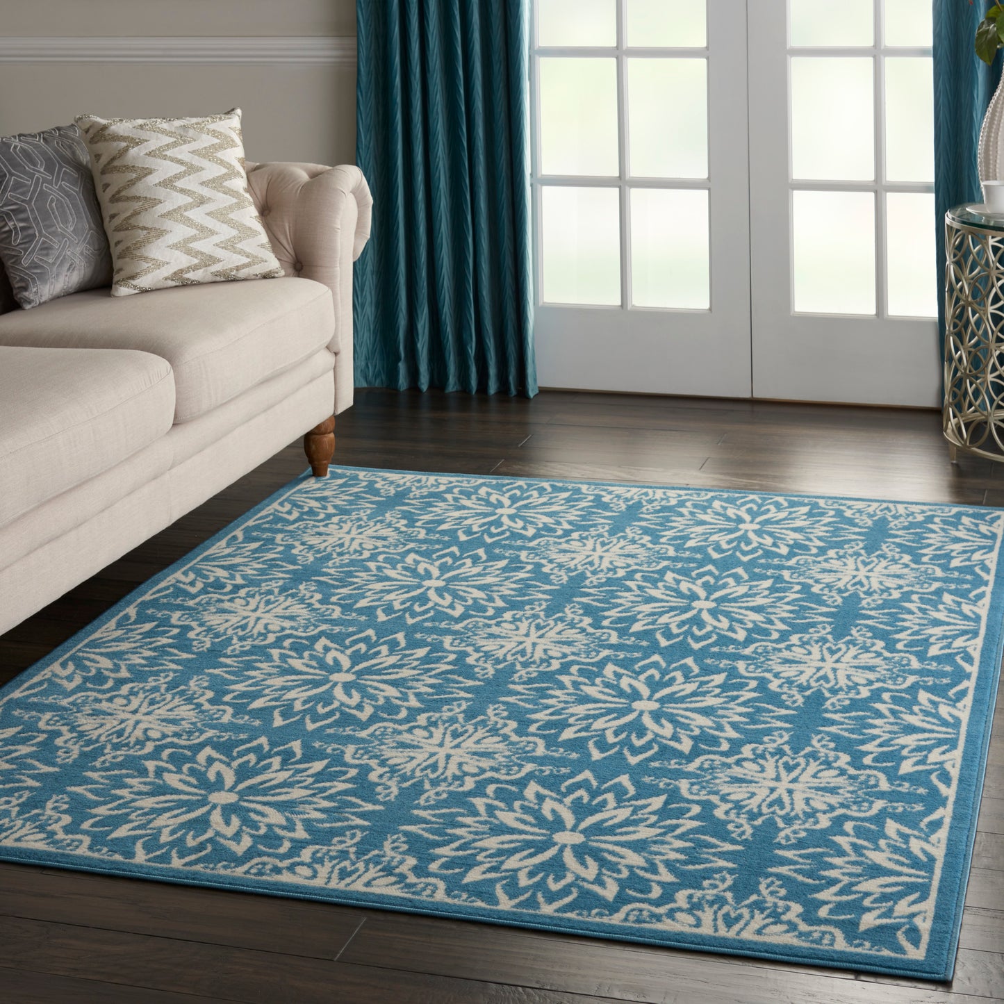 Blue rug with cream floral pattern and border in a living room with beige sofa and teal curtains.