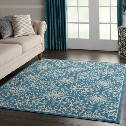 Blue rug with cream floral pattern and border in a living room with beige sofa and teal curtains.