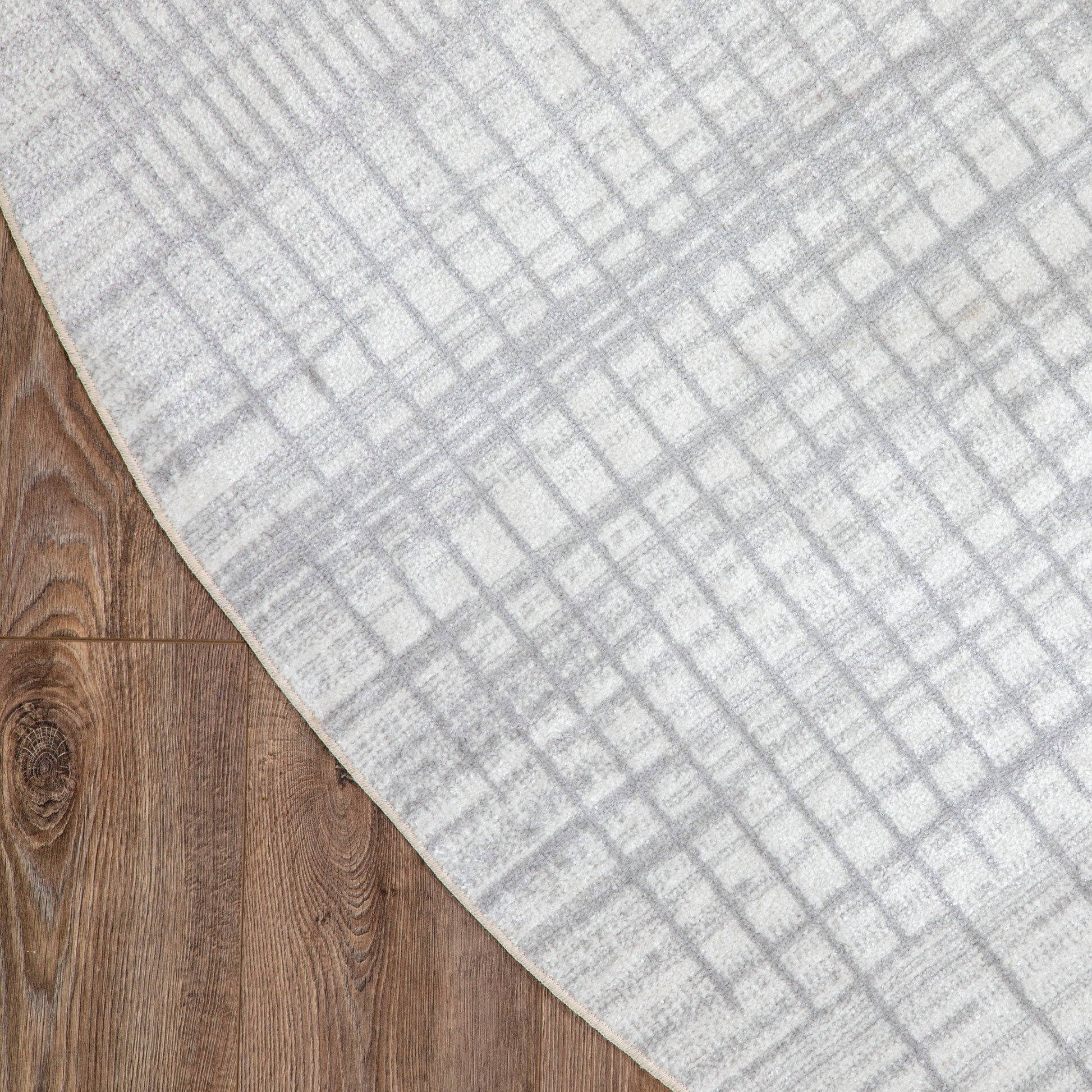 Light gray woven round rug with a subtle grid pattern on a wooden floor; mid-century modern geometric style.