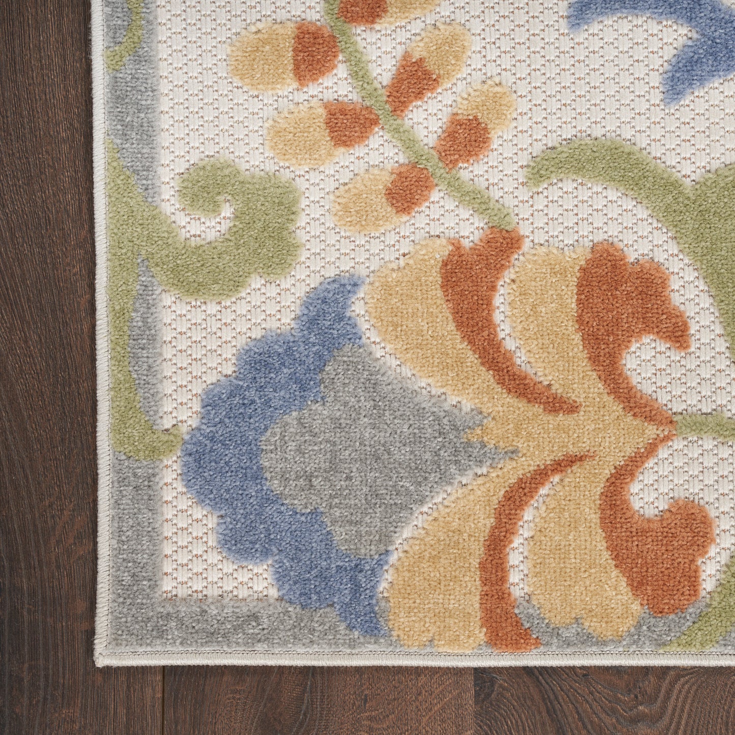 Corner of a floral area rug with beige base, orange, yellow, blue and gray blooms, and light gray border.