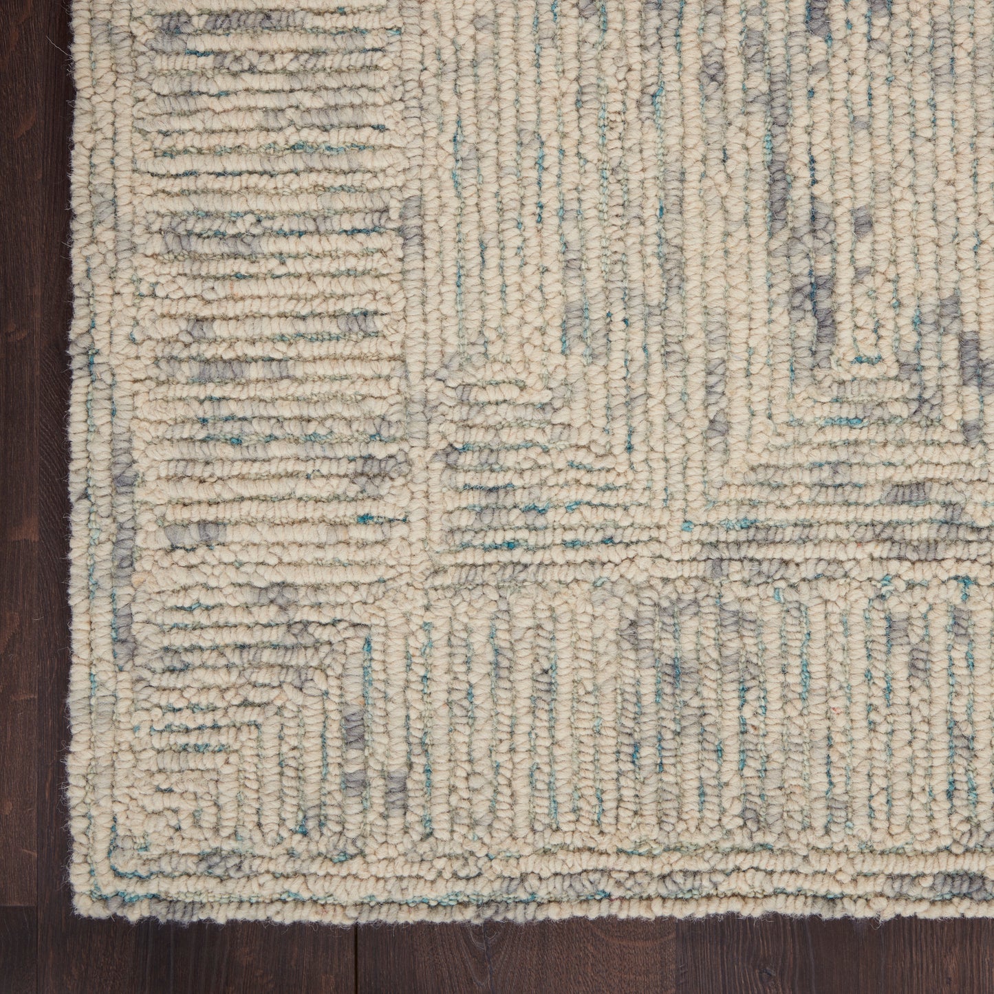 Ivory chunky-loop area rug with pale blue and gray geometric pattern on dark wood floor.