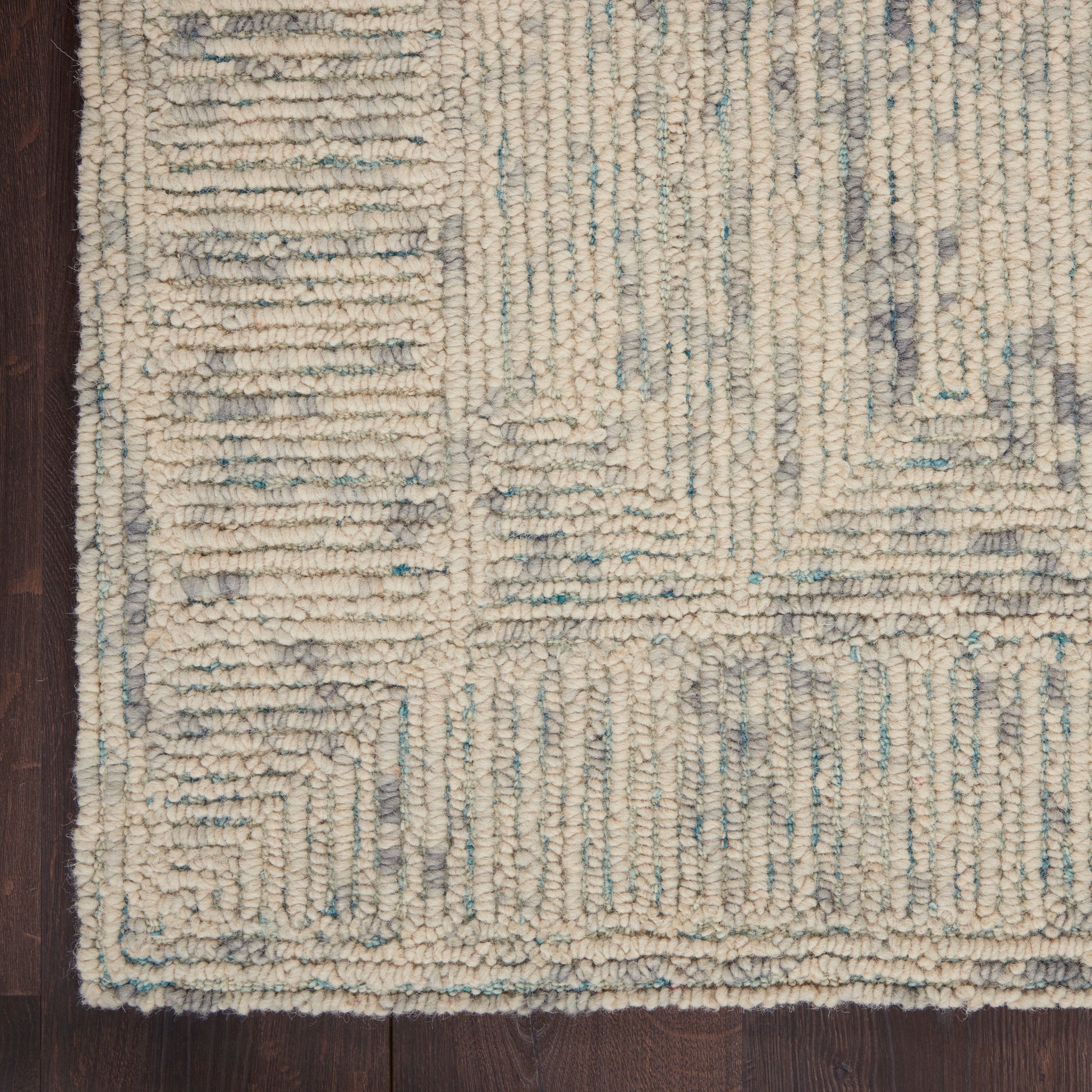 Ivory chunky-loop area rug with pale blue and gray geometric pattern on dark wood floor.
