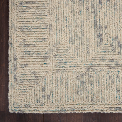Ivory chunky-loop area rug with pale blue and gray geometric pattern on dark wood floor.