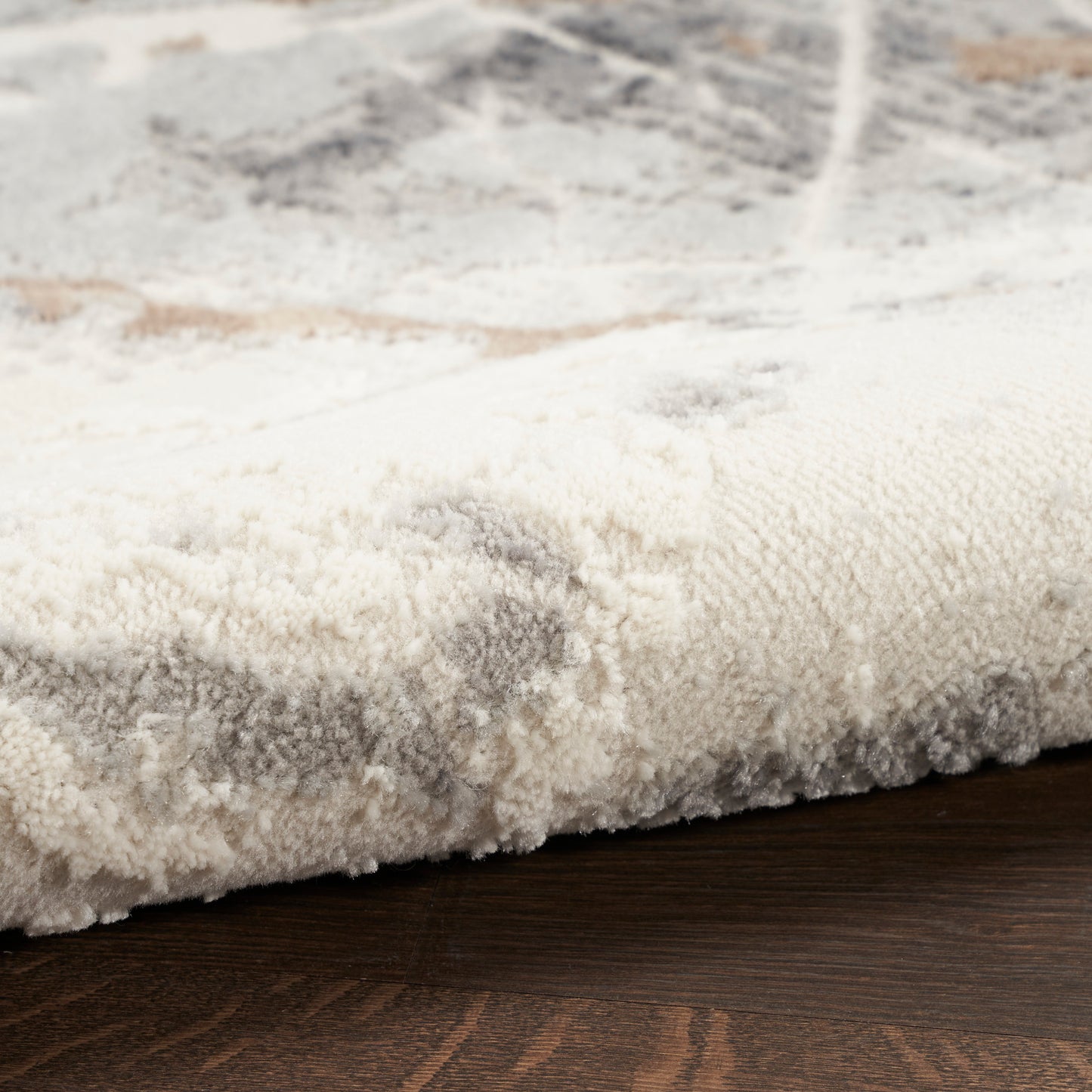 Close-up of a cream-gray plush area rug with a subtle pattern on dark wood floor.