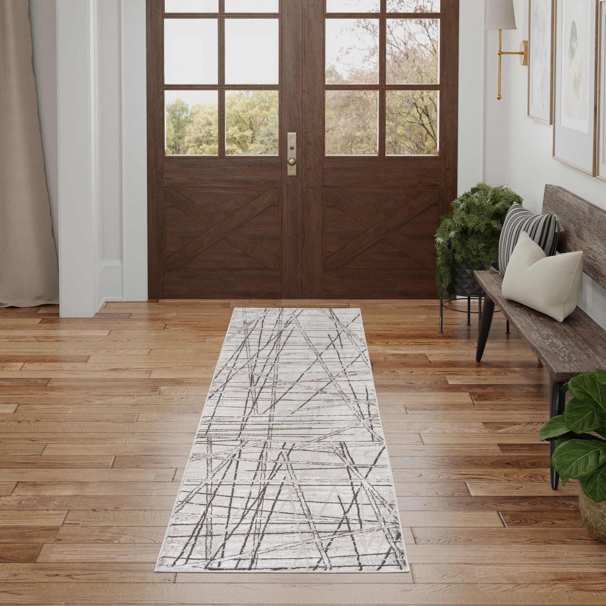 Dark wood double doors with glass panes, light hardwood floor, 8' gray abstract runner rug, entryway bench and plants.