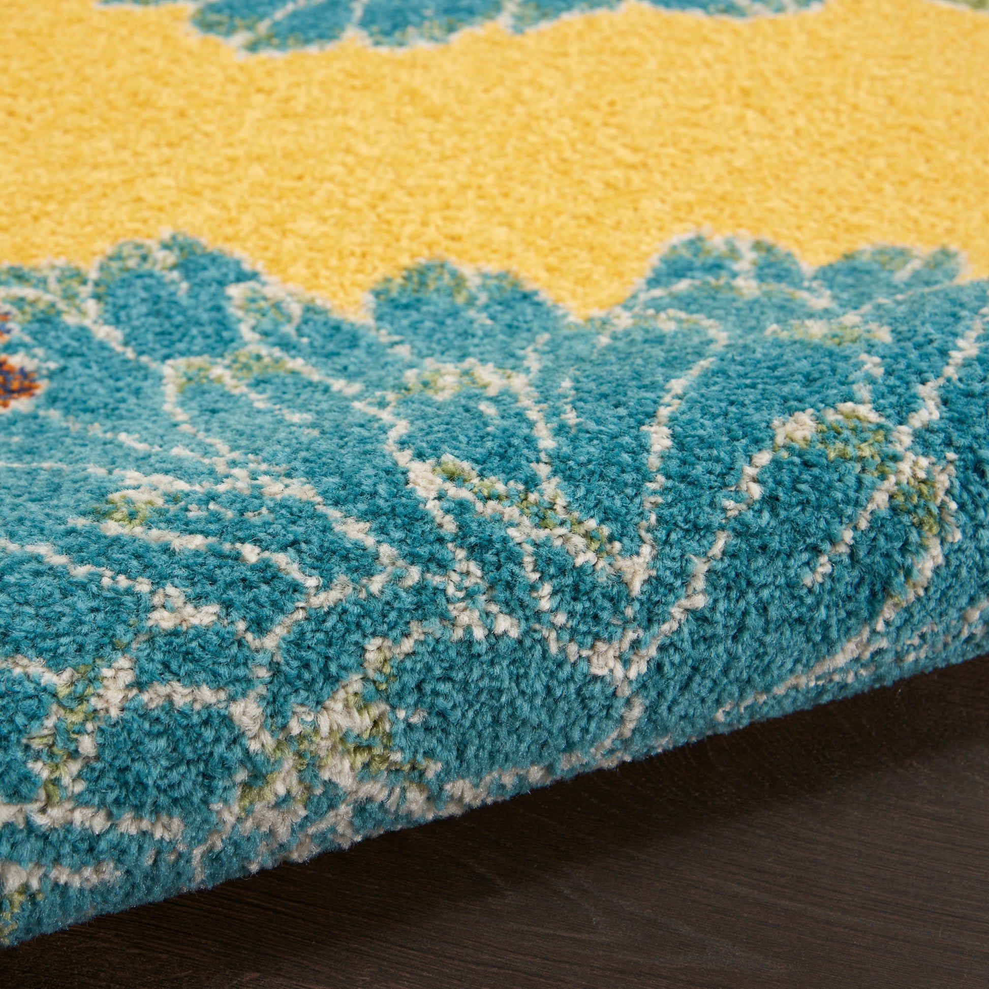 Close-up of teal-blue and yellow floral rug edge with plush pile on dark wood floor.