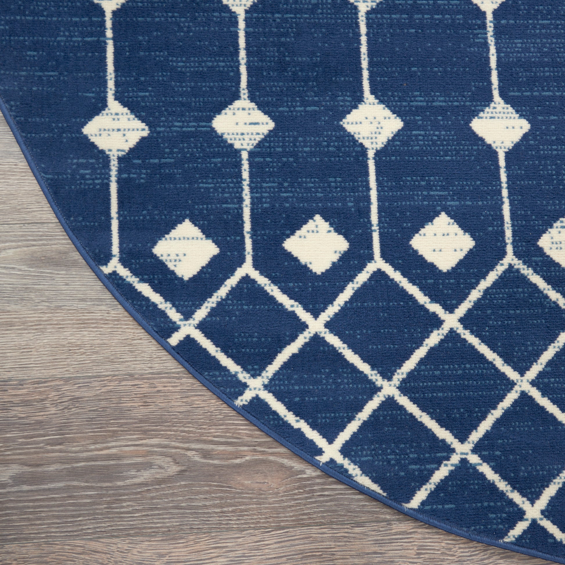 Blue rug with white geometric lattice and diamond motifs; curved edge on wooden floor.