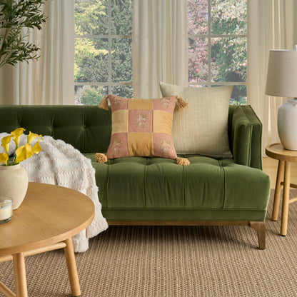 Olive green velvet tufted sofa with pink-yellow plaid cushion with tassels, beige throw, round wooden coffee table.