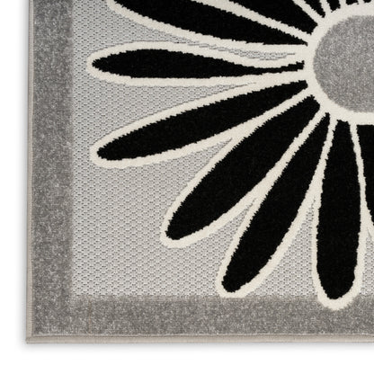 Close-up of gray rug with bold black flower petals outlined in cream and a light border; textured weave.