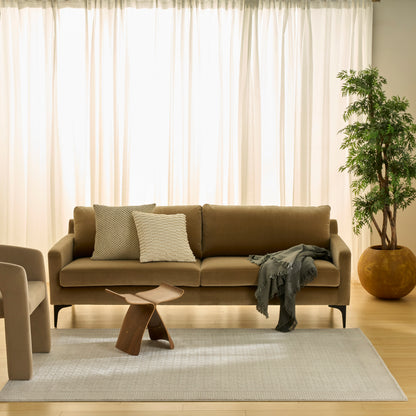 Neutral modern rug (4' x 6') beneath a sculptural wooden coffee table in a beige living room with a beige sofa, textured pillows, gray throw, and a potted plant by sheer curtains.