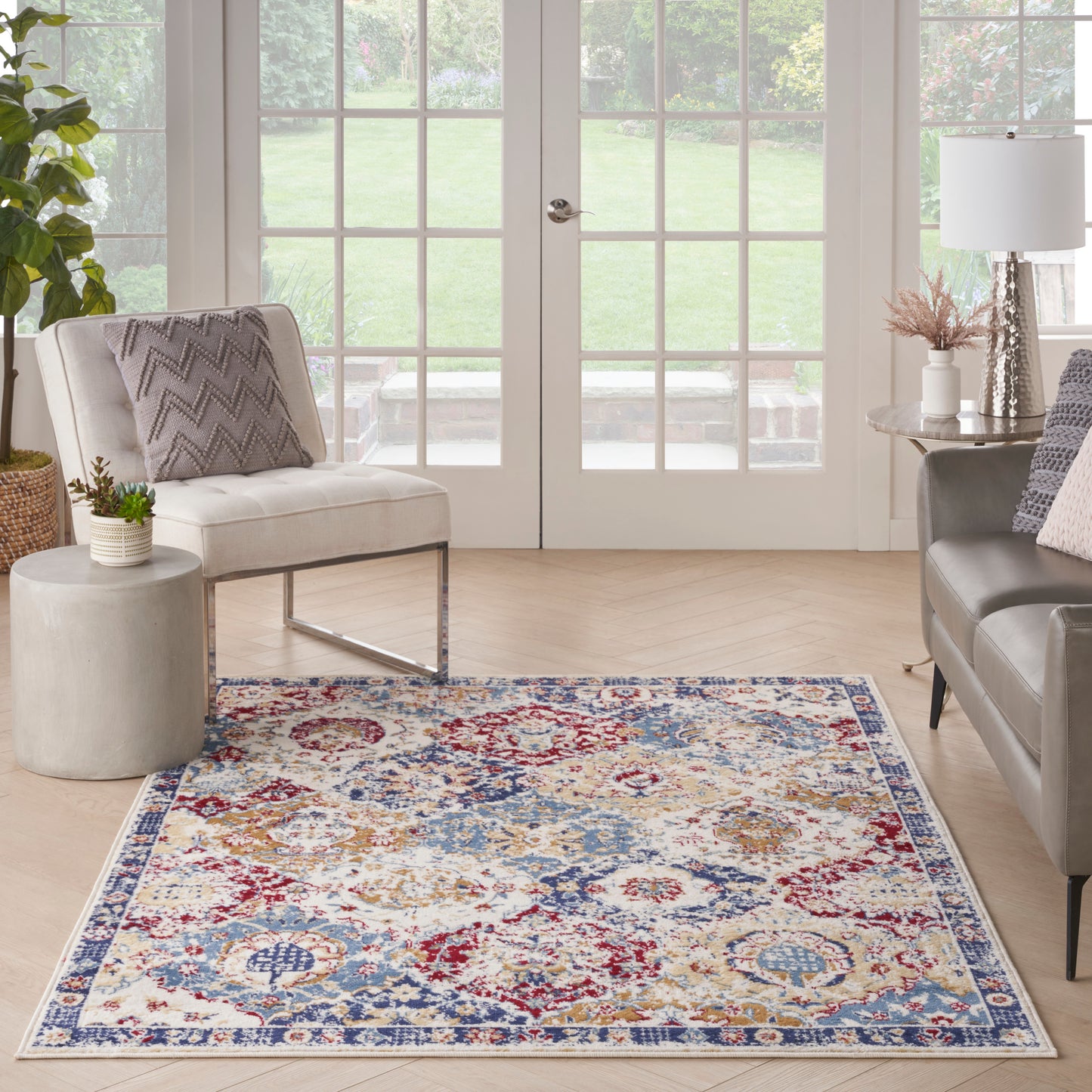 Patterned area rug in blue, red, ivory tones under a bright living room with cream chairs.