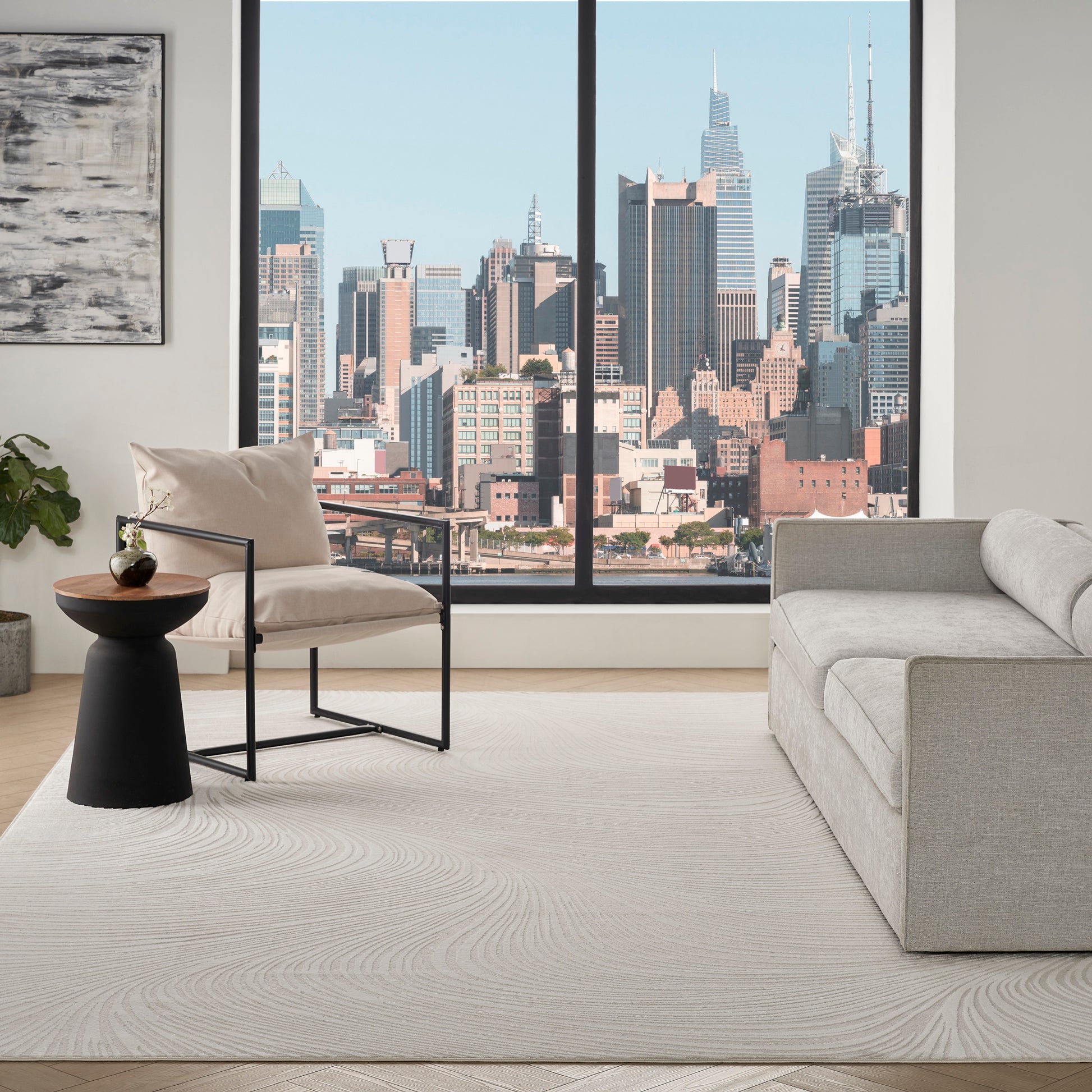 Modern living room: light gray sofa, beige armchair with black frame, round black table, plant, abstract art, skyline view.