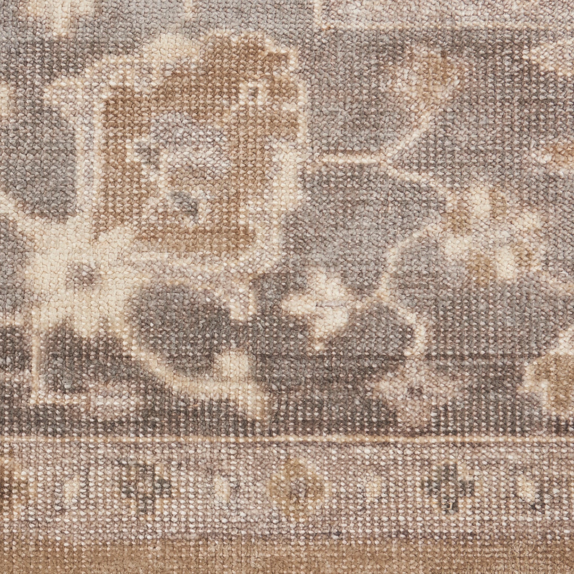 Neutral woven rug close-up with beige and taupe floral pattern and decorative border.