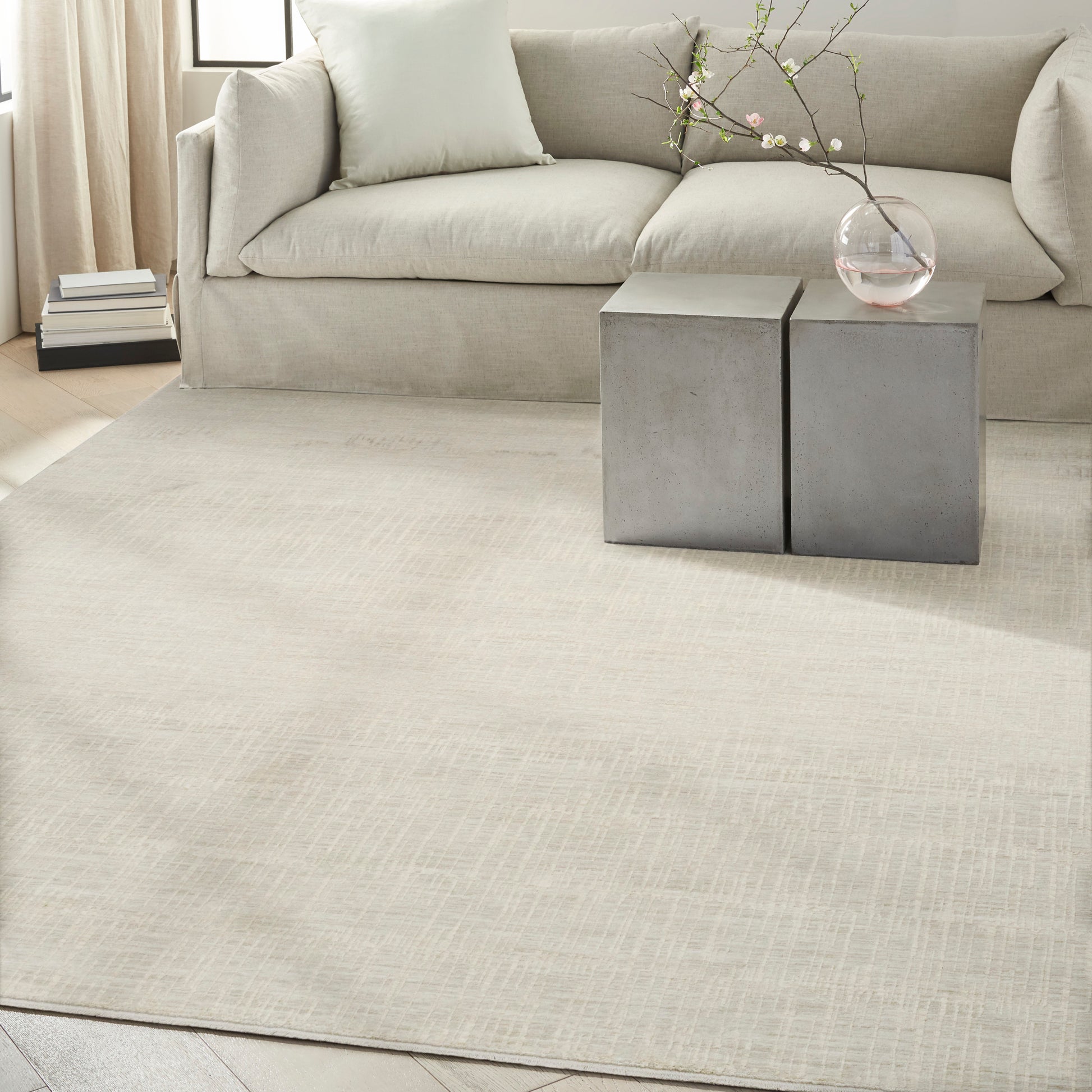 Neutral living room with beige sofa, cream rug, two gray concrete block side tables, glass vase with blossoming branches.