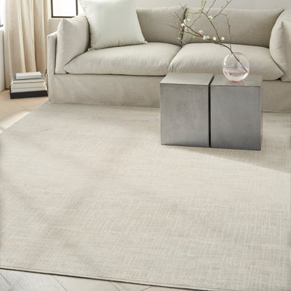 Neutral living room with beige sofa, cream rug, two gray concrete block side tables, glass vase with blossoming branches.