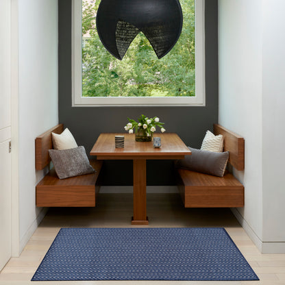 Built-in wooden dining nook with two benches, square table, navy chevron rug, black pendant lamp, and flowers by window.