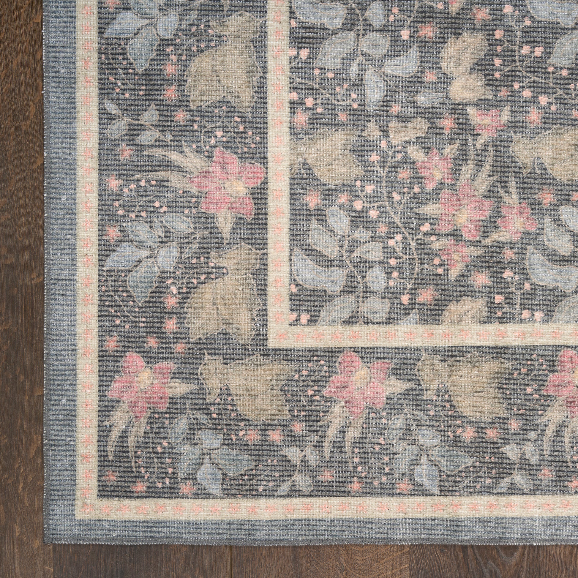 Rectangular navy area rug with pink flowers and cream vines; pale border stripes on a dark wood floor.