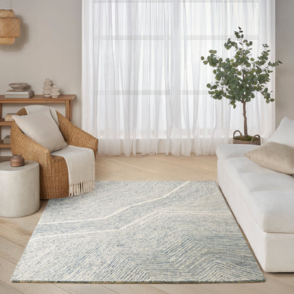Bright living room with blue-gray patterned rug, white sofa, wicker armchair & cream throw, sheer curtains.