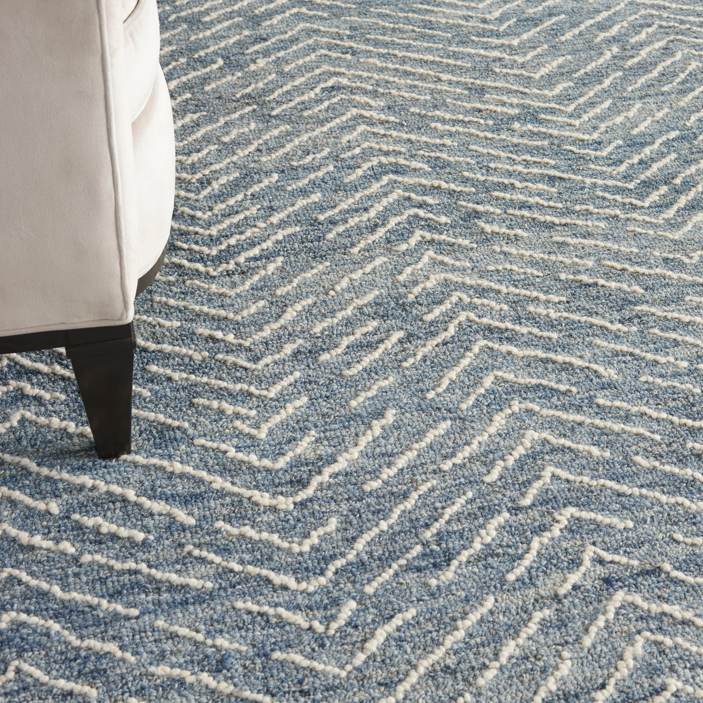 Cream sofa leg on dark wood, resting on a blue and white chevron patterned rug with raised loop fibers.