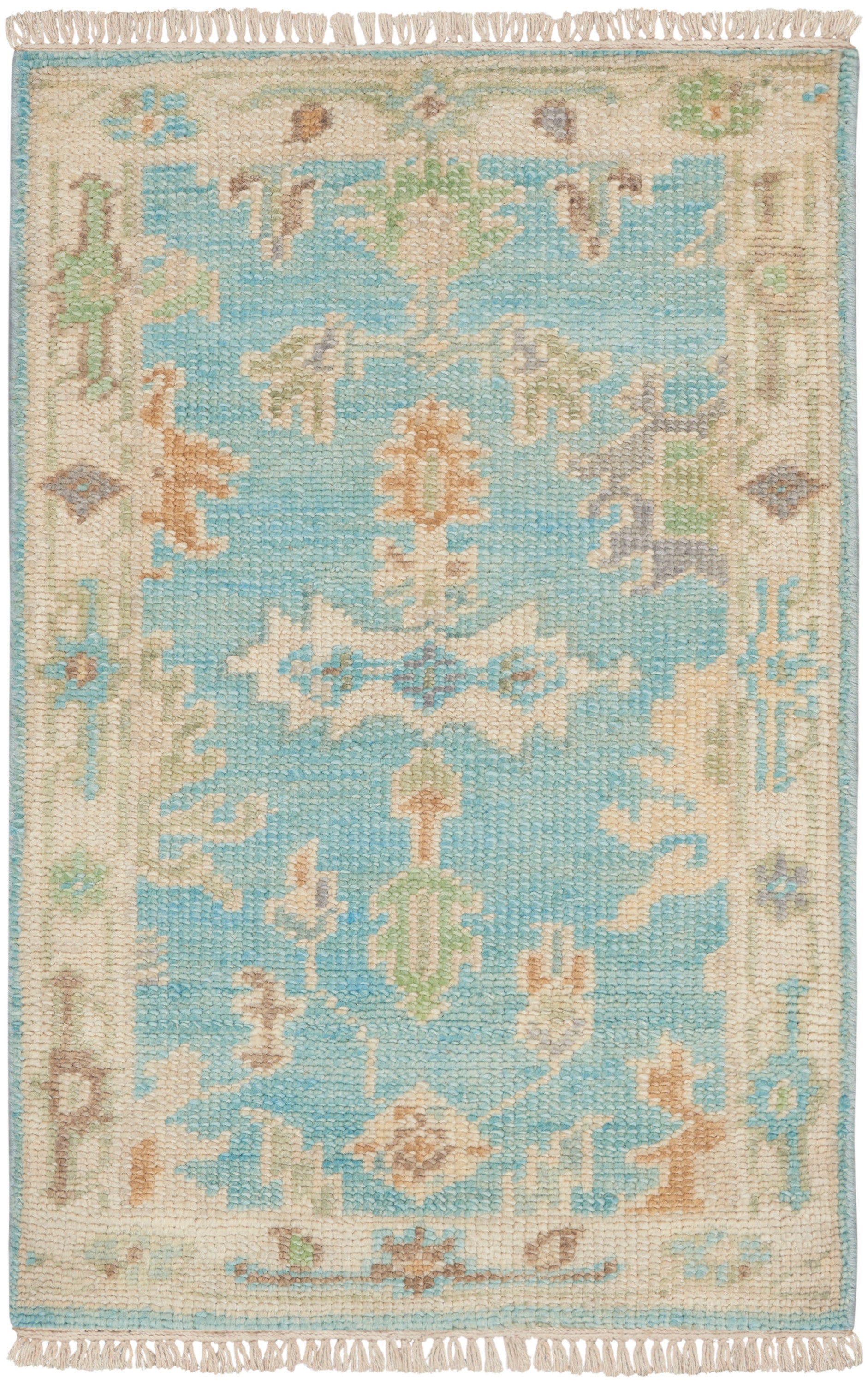 Rectangular woven rug with turquoise center, cream-beige border, pastel floral motifs and fringed ends.