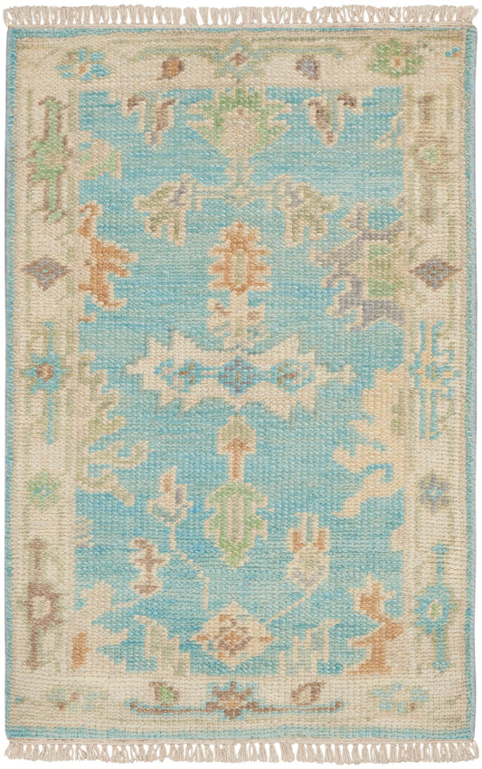 Rectangular woven rug with turquoise center, cream-beige border, pastel floral motifs and fringed ends.