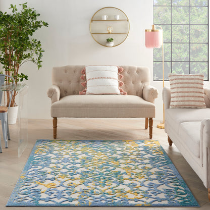 Living room with blue-yellow area rug, beige tufted sofa, pink striped pillows, round wall shelf, pink lamp, grid window.