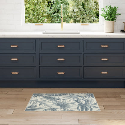Dark navy cabinets with copper pulls, white countertop, brass faucet, potted plant, and blue palm-leaf rug on wood floor.