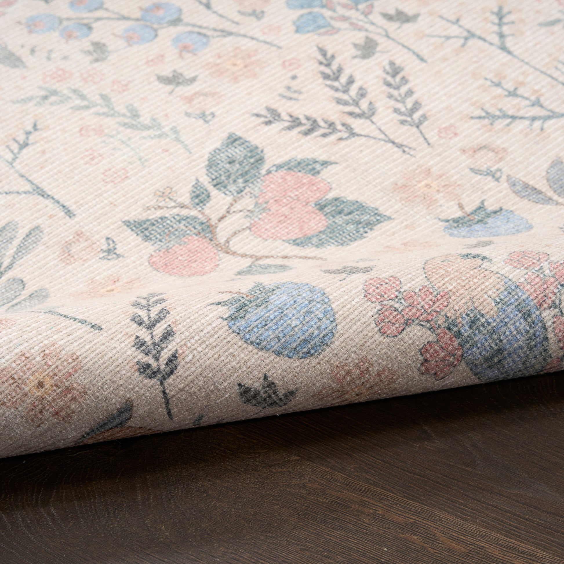 Pastel floral woven fabric with pink, blue, and green blooms on beige background, folded over dark wood surface