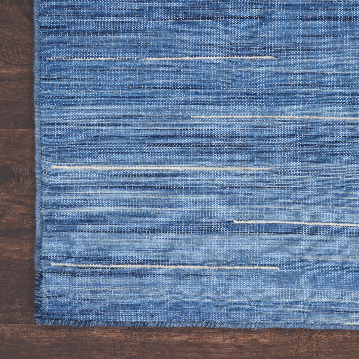 Blue woven rectangular rug with subtle white horizontal stripes, flat-weave, casual modern style, on wooden floor.