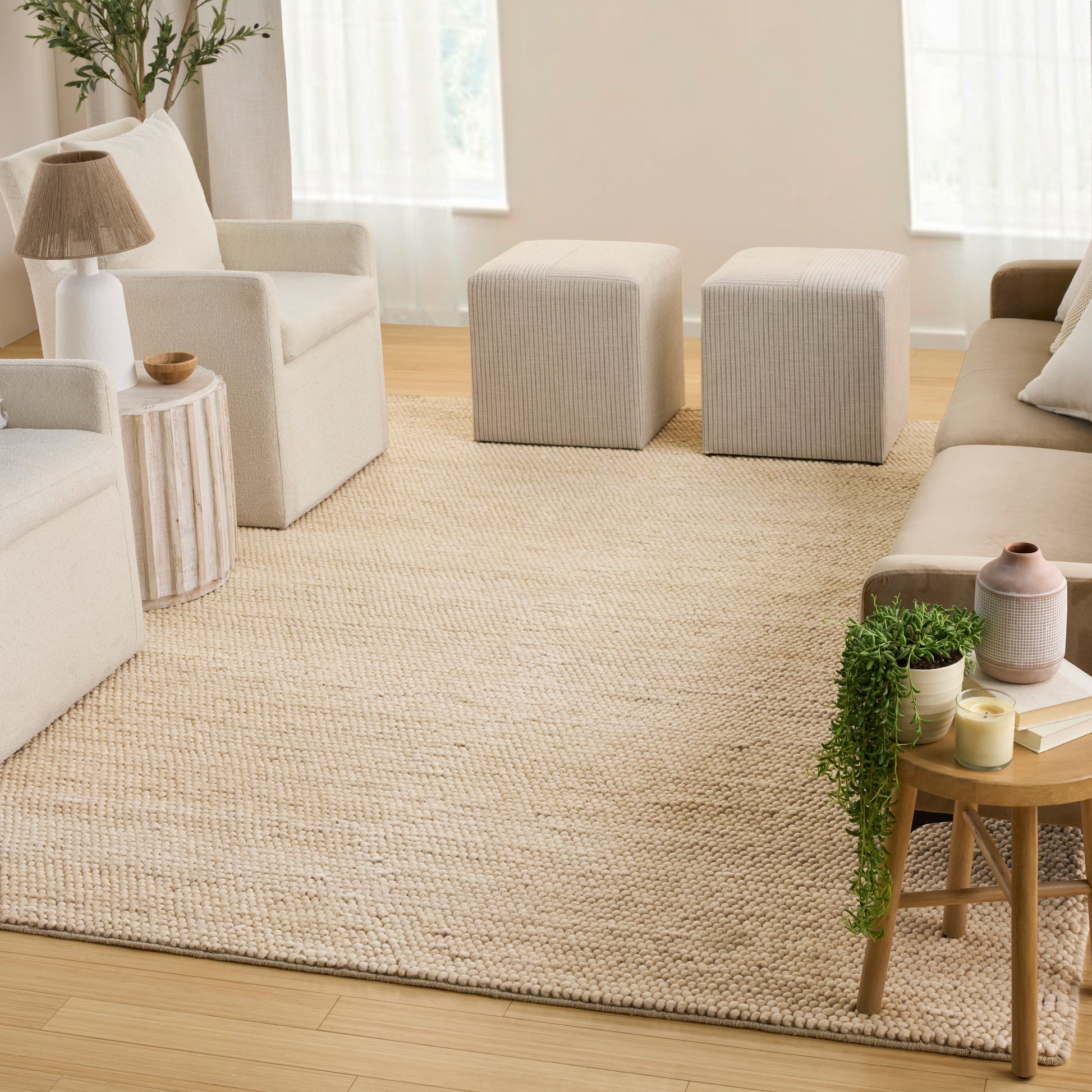 Neutral living room with cream ivory seating, two square beige ottomans, woven jute rug, wood side tables and green plants.
