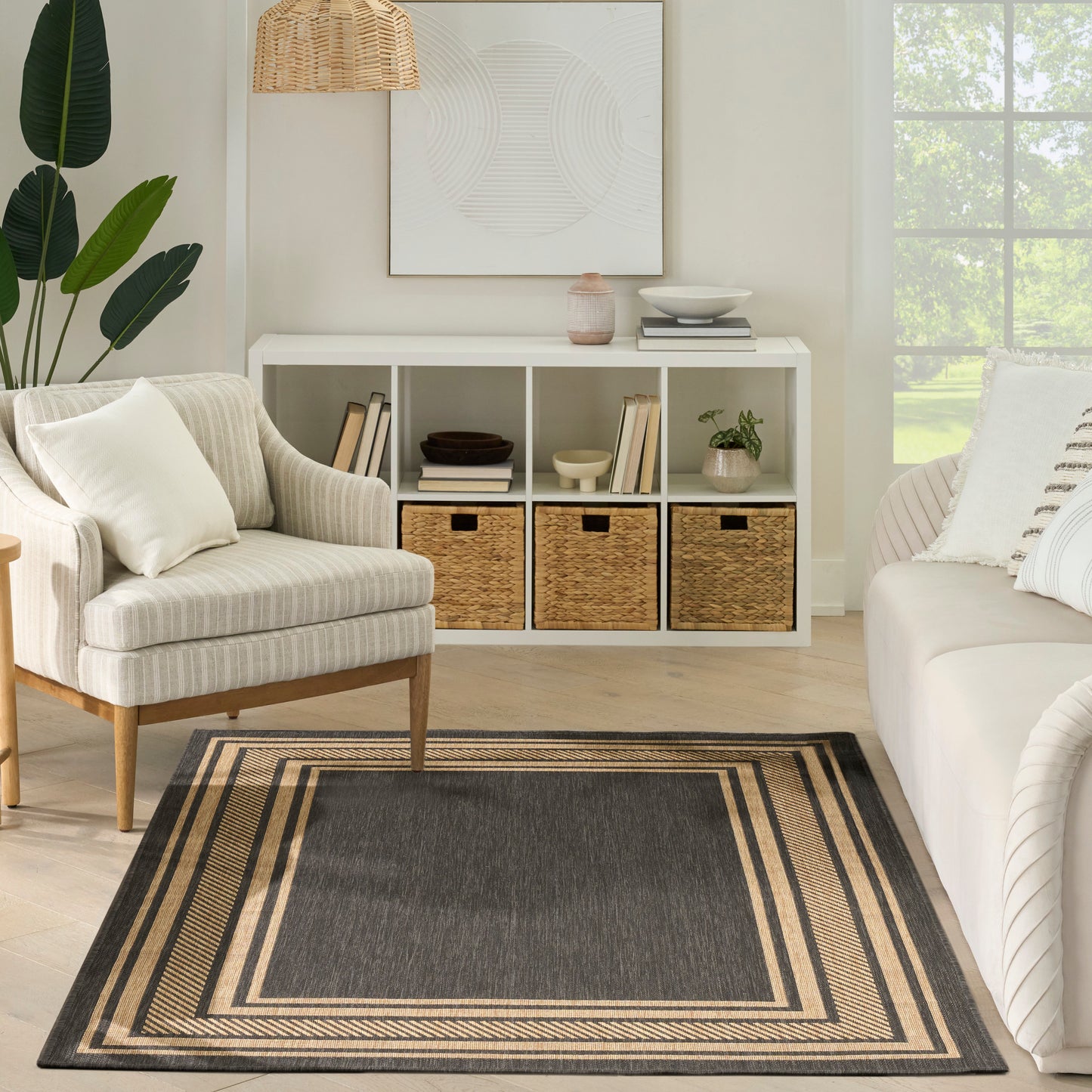 Neutral living room with white cubby storage, wicker baskets, beige striped armchair, sofa, plant, woven pendant light, framed abstract art, and a layered border rug.