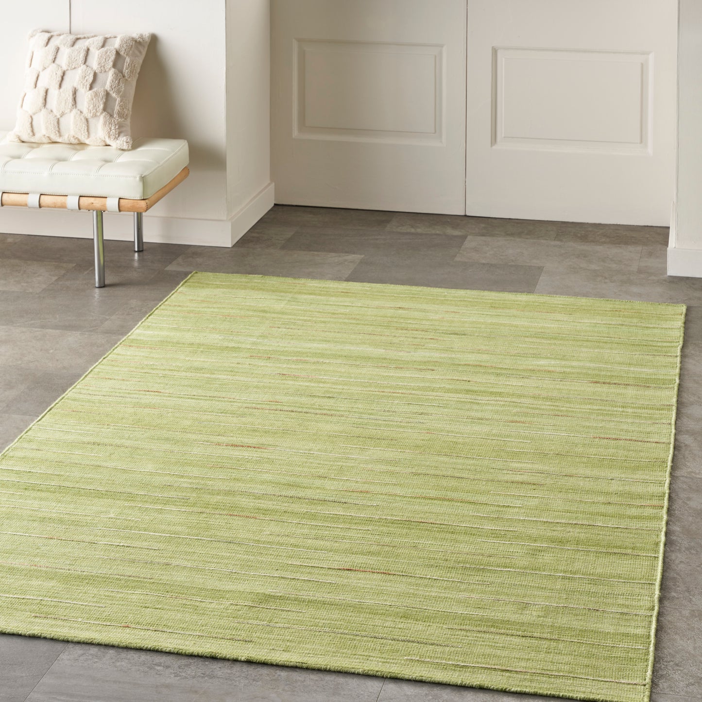 Light lime-green rectangular area rug with subtle horizontal stripes in a modern entryway beside a white cushioned bench.