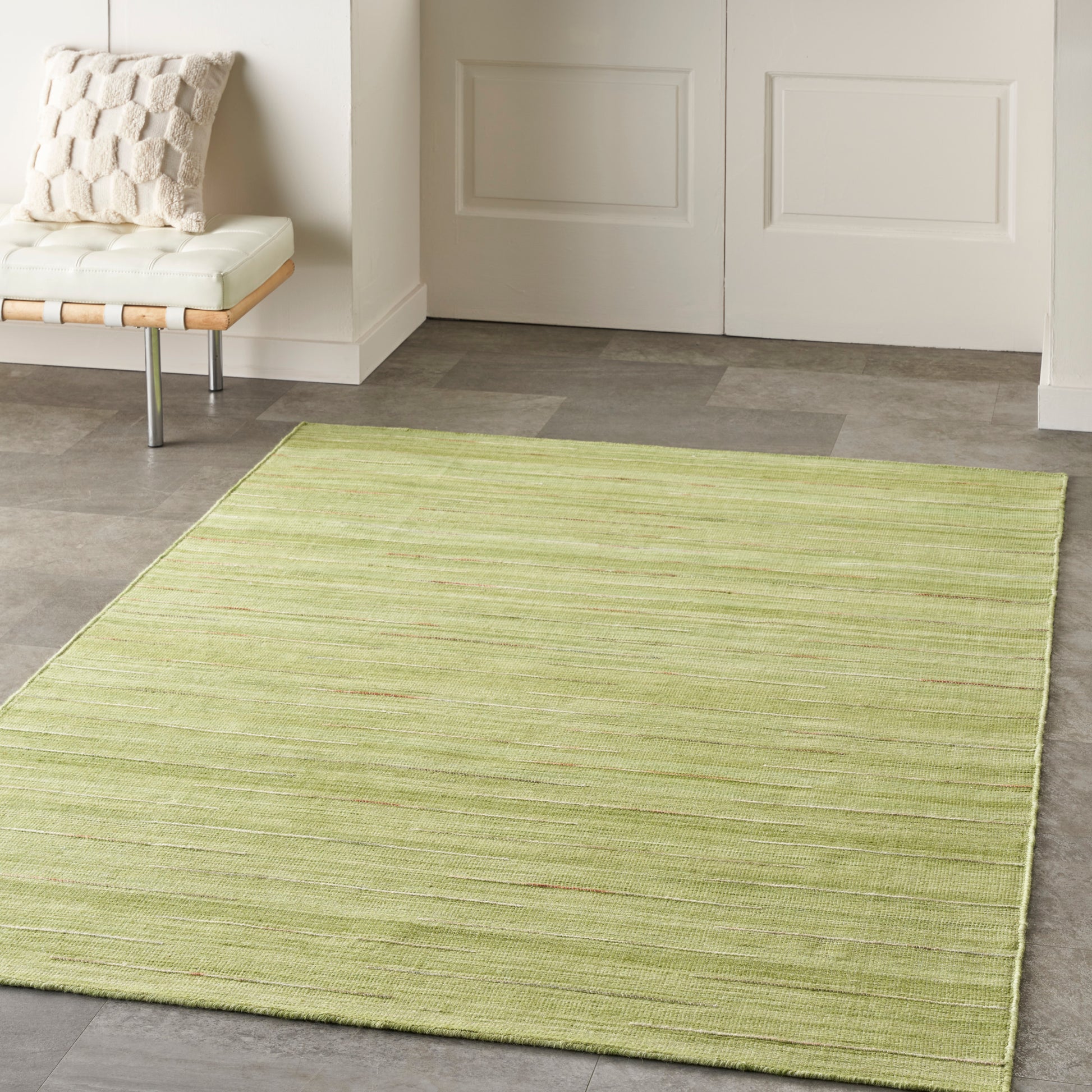 Light lime-green rectangular area rug with subtle horizontal stripes in a modern entryway beside a white cushioned bench.