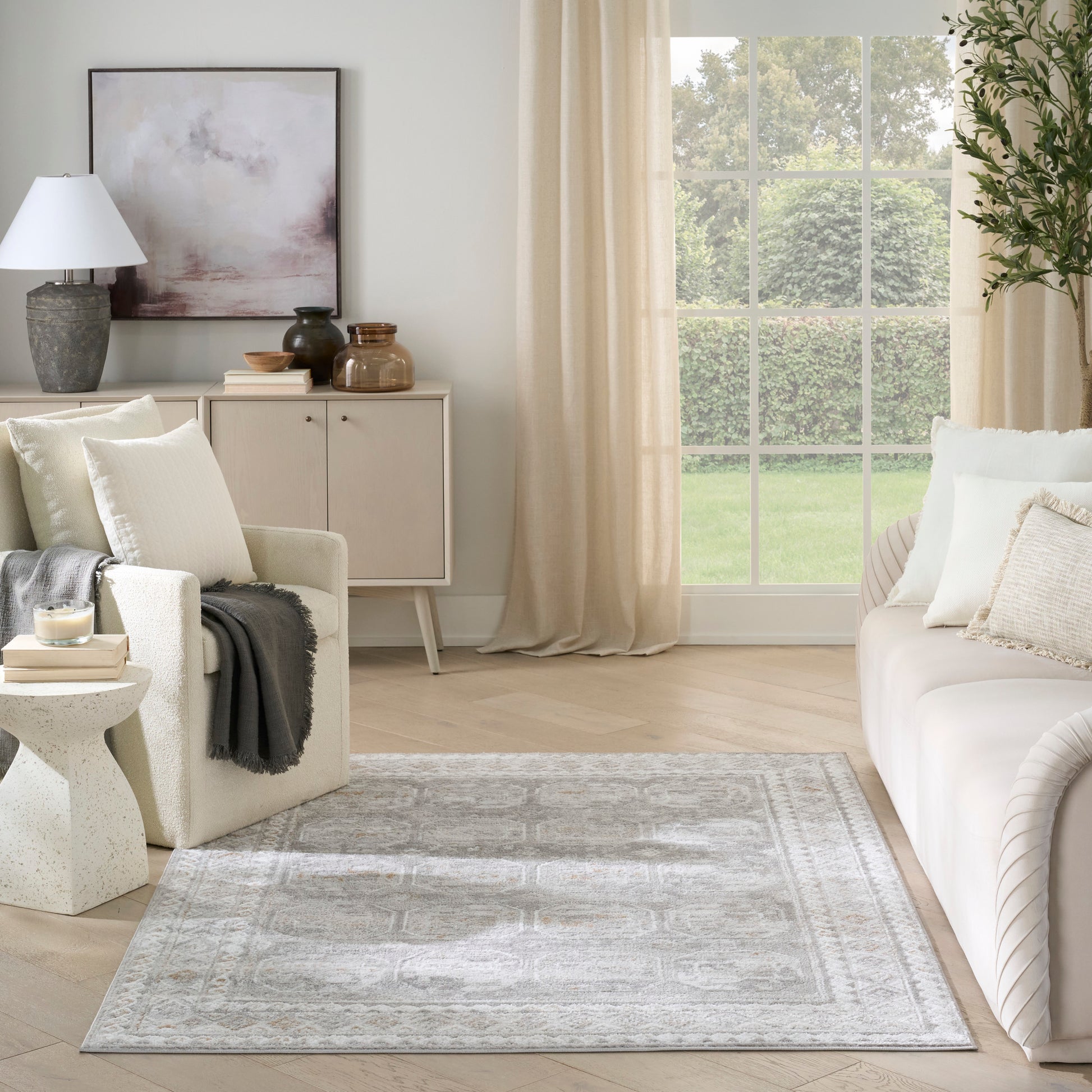 Neutral living room with cream sofa, beige curtains, light wood cabinet, abstract artwork, and a soft gray patterned area rug.