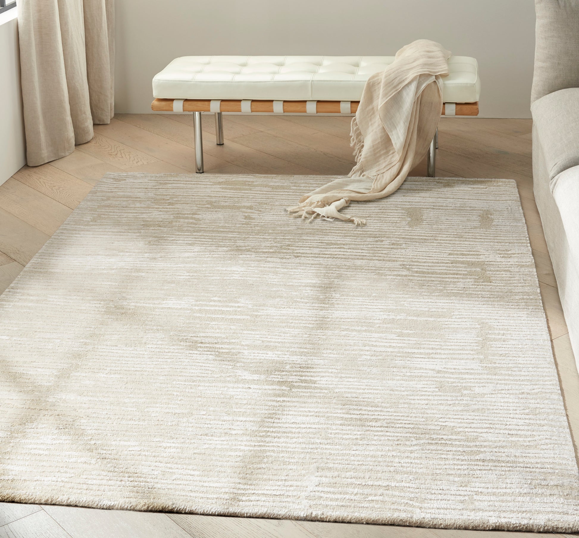 Cream-beige plush area rug with subtle linear texture, anchors seating in a light modern living room.