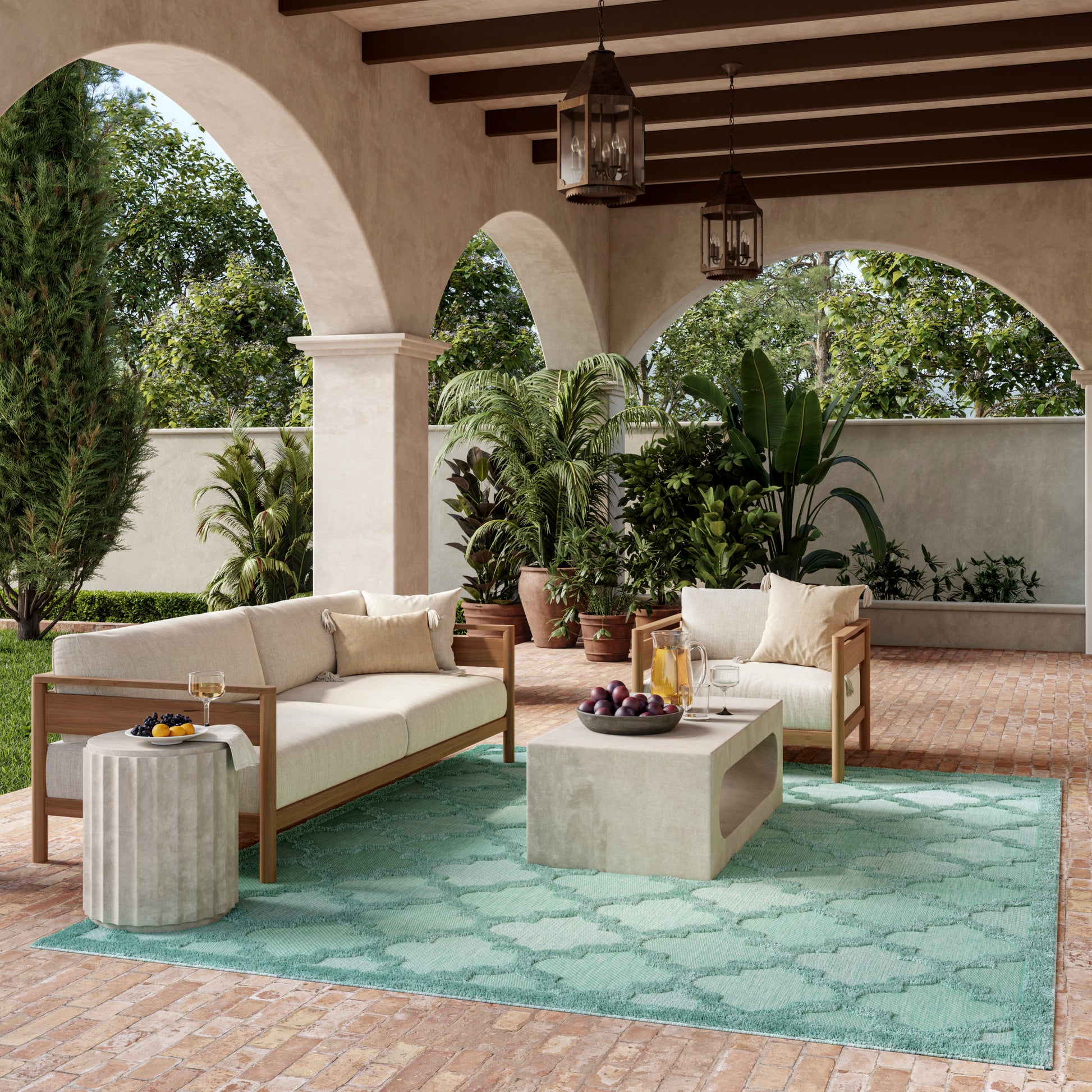 Outdoor patio with arched stucco arches, cream cushioned seating, concrete coffee table, turquoise rug, potted plants.