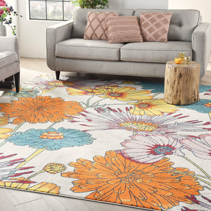 Living room with a vibrant floral rug featuring orange, yellow, blue flowers, a gray sofa with pink pillows, and a wooden stump table.