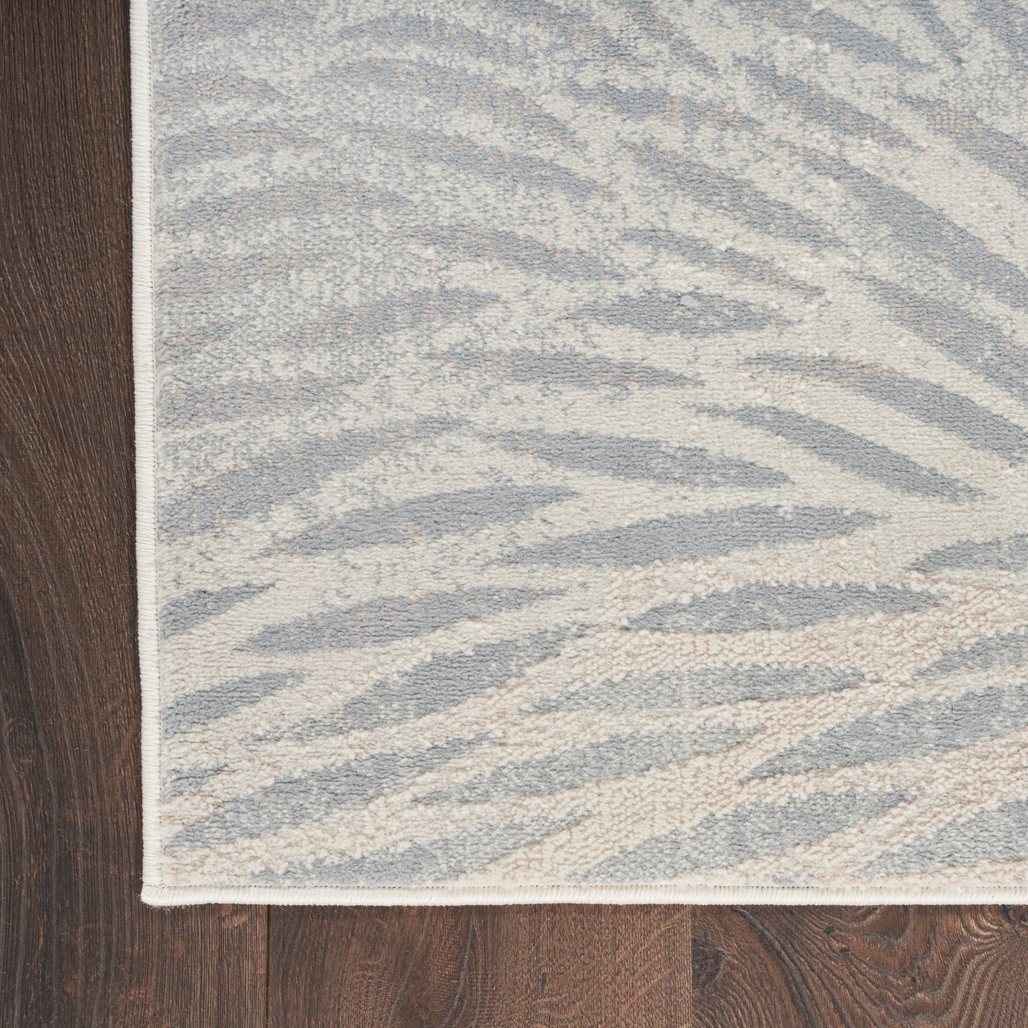Gray and ivory zebra-print rug with white binding edge on dark wooden floor.