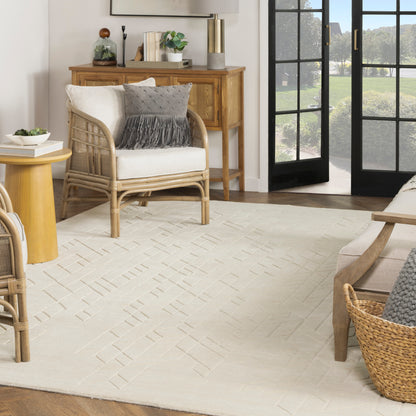 Cream woven rug with a light geometric pattern, 10' x 14', in a living room with a wooden console & glass doors; seating area features white cushions & gray pillows.