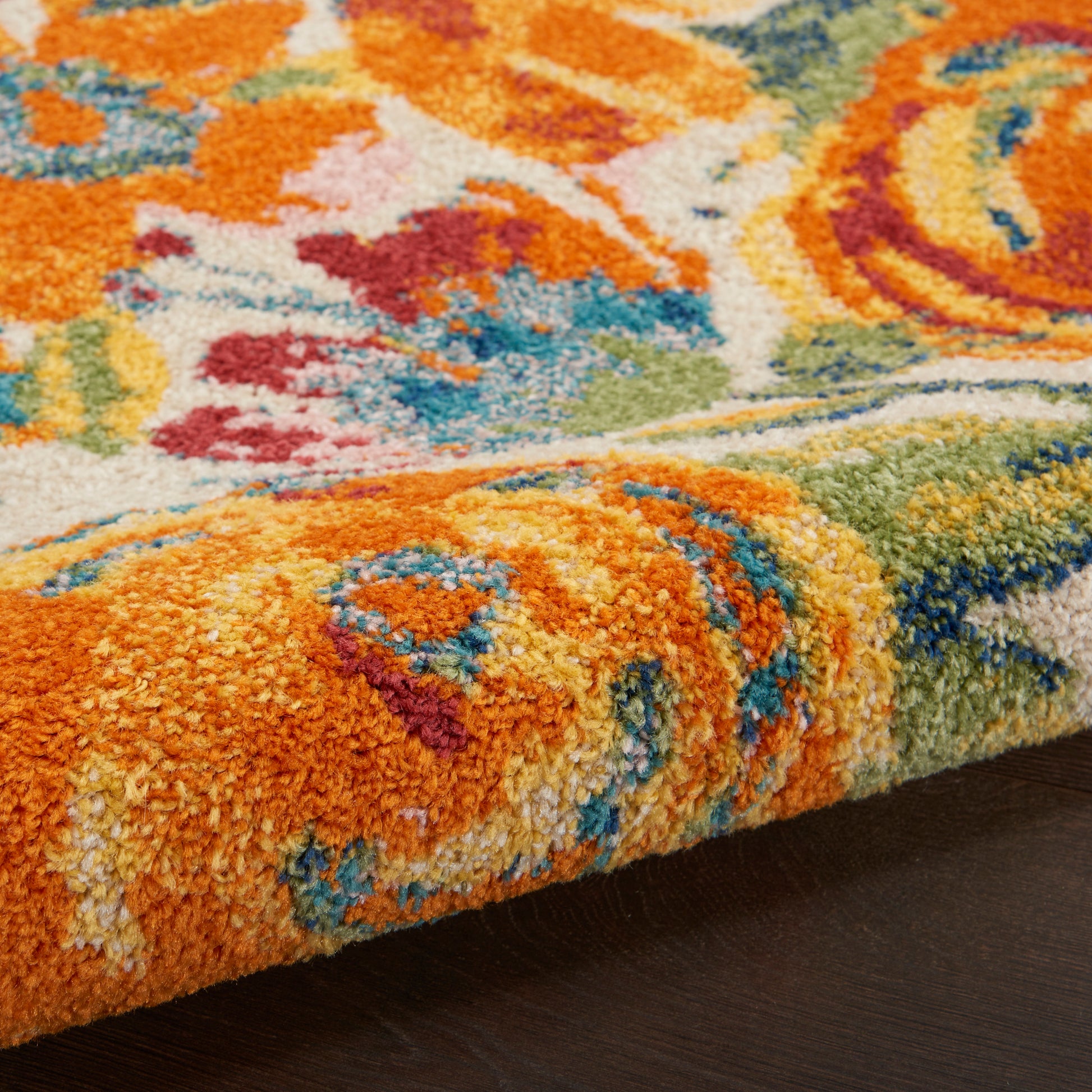 Vibrant floral shag rug with thick pile in orange, blue, green and yellow on dark wood floor.