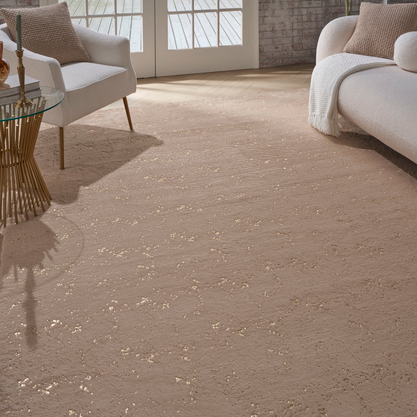 Cozy living room with beige plush rug, white sofa and armchair, glass side table with gold base, brick wall.