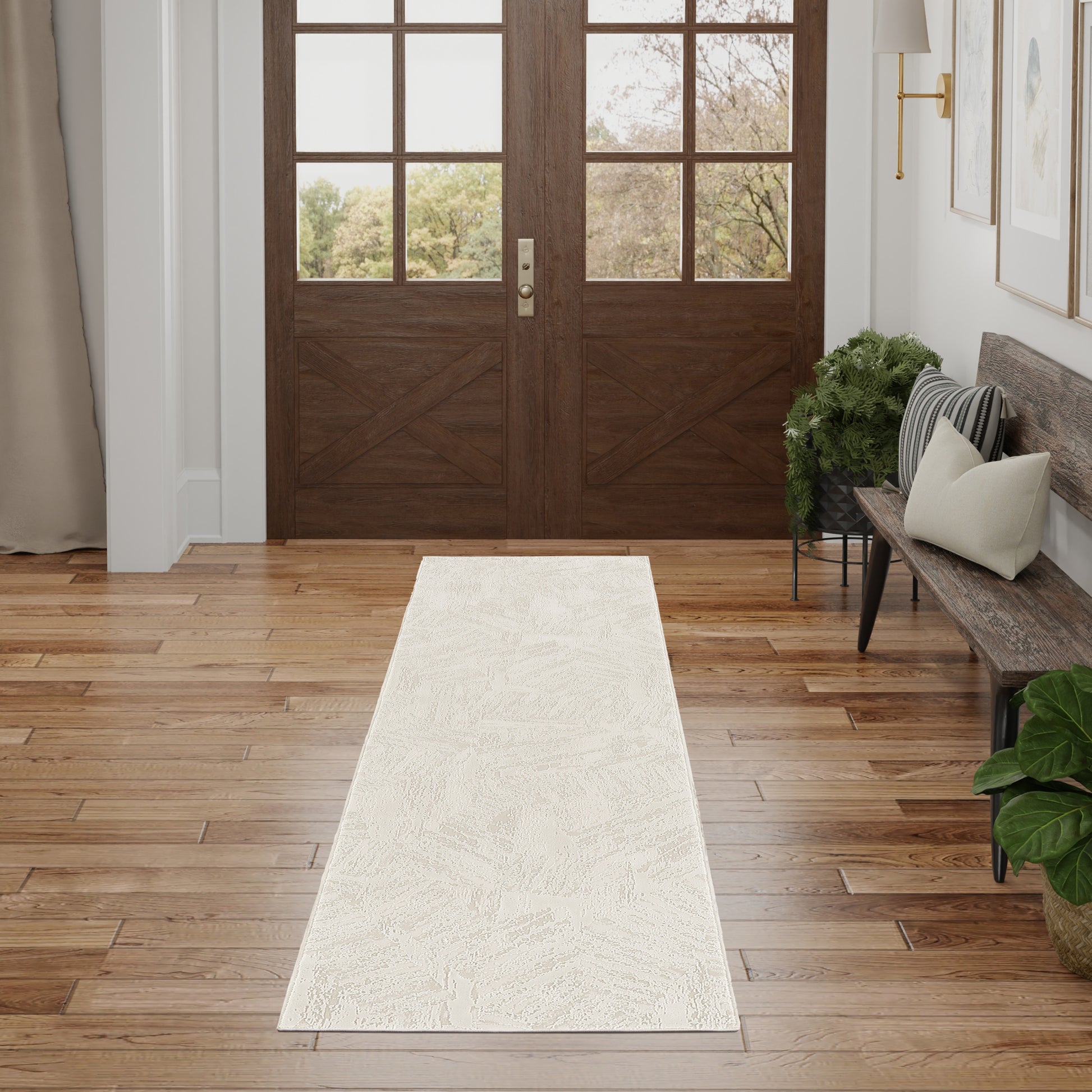 Dark wood double entry doors with grid glass, cream patterned runner rug on hardwood floor, bench with pillows and greenery.