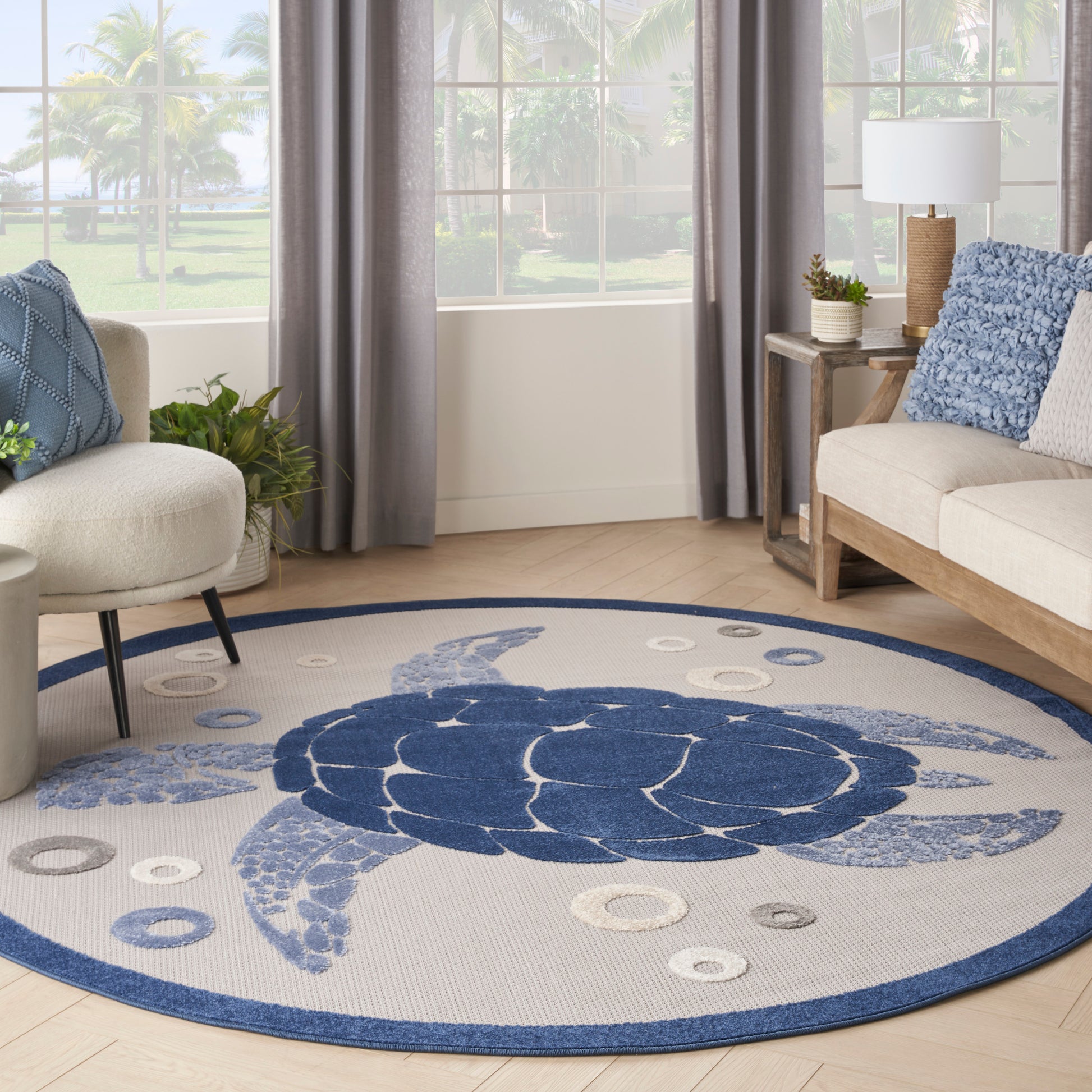 Round coastal rug with navy turtle motif on light gray field, blue border, in a bright living room.
