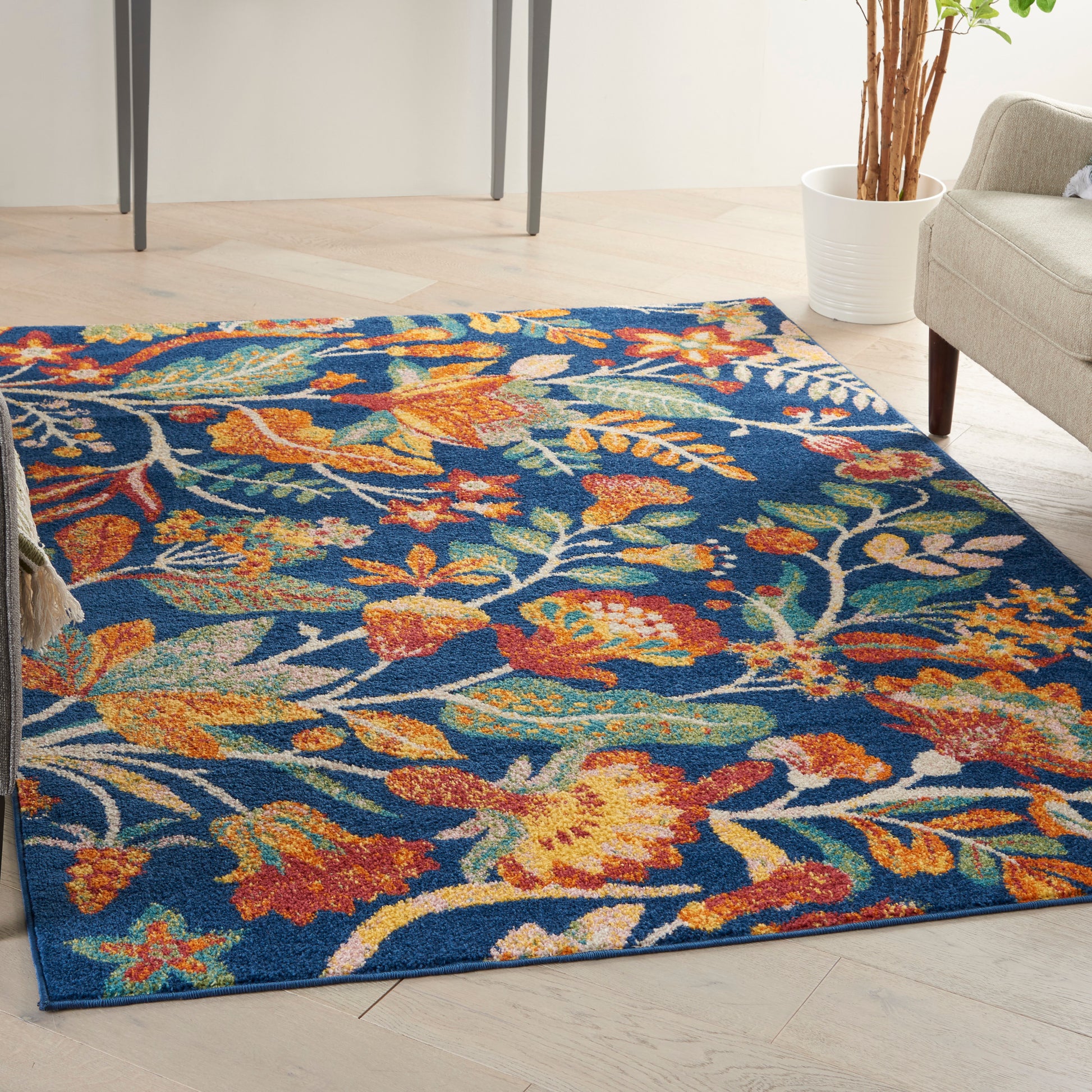 Vibrant floral area rug with orange, yellow, teal, and white blossoms on a deep blue background in a modern living room.