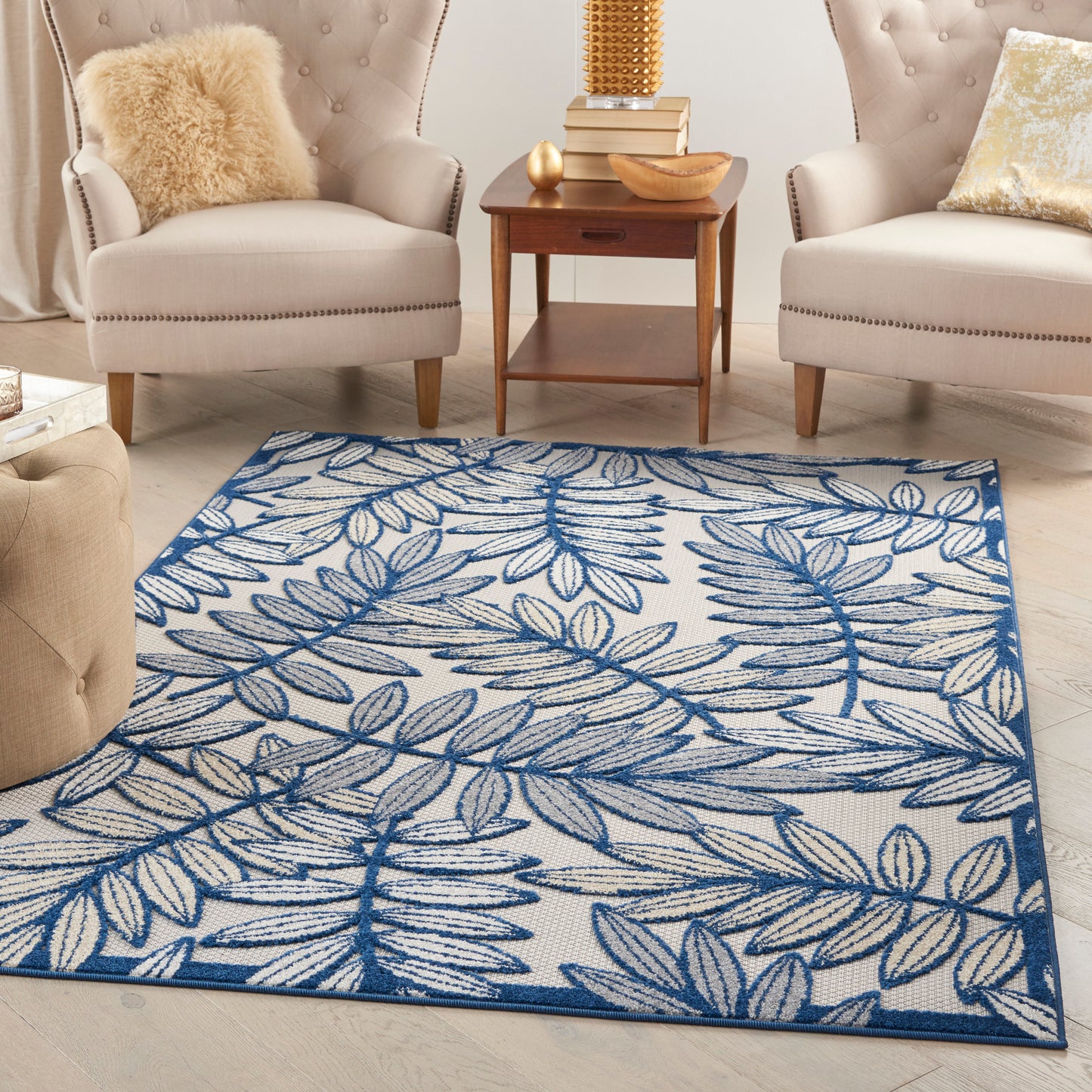 Blue botanical leaf-pattern area rug on a cream background in a beige living room with tufted chairs.