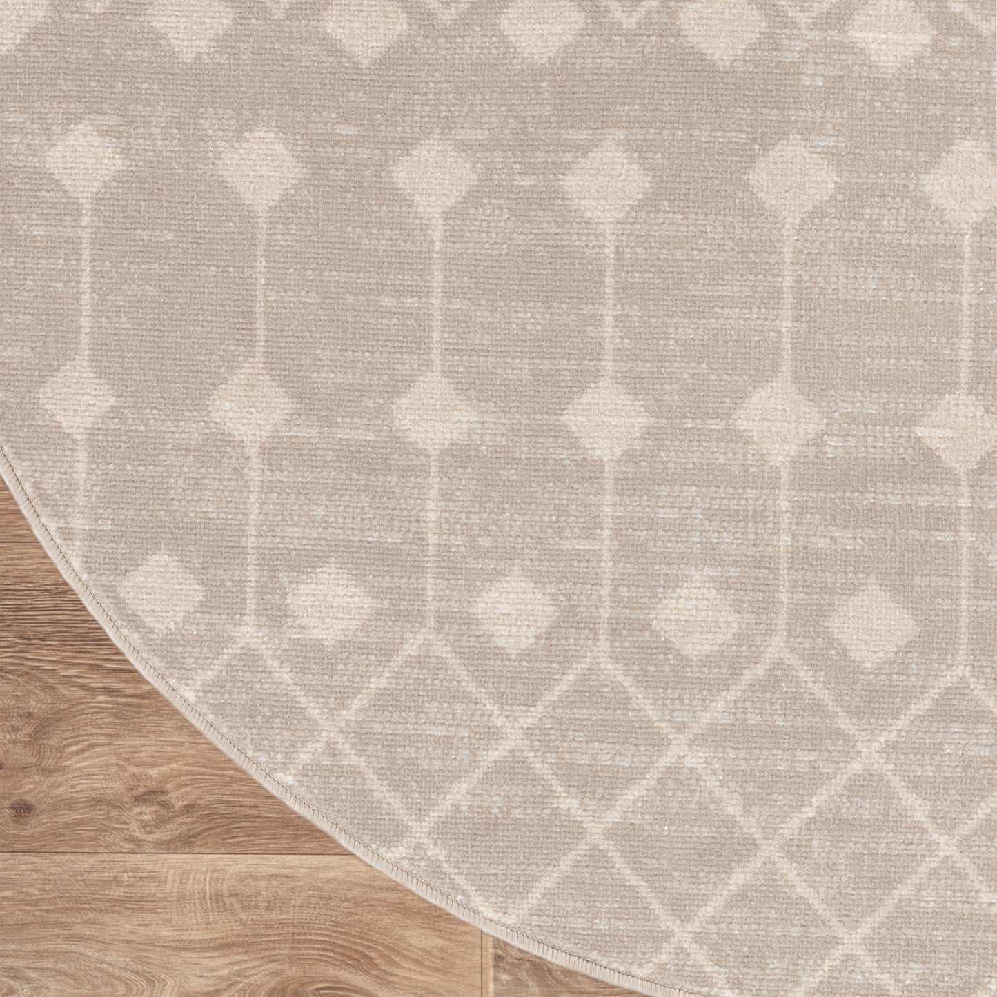 Beige geometric area rug with diamond lattice pattern on light wood floor; curved edge visible.