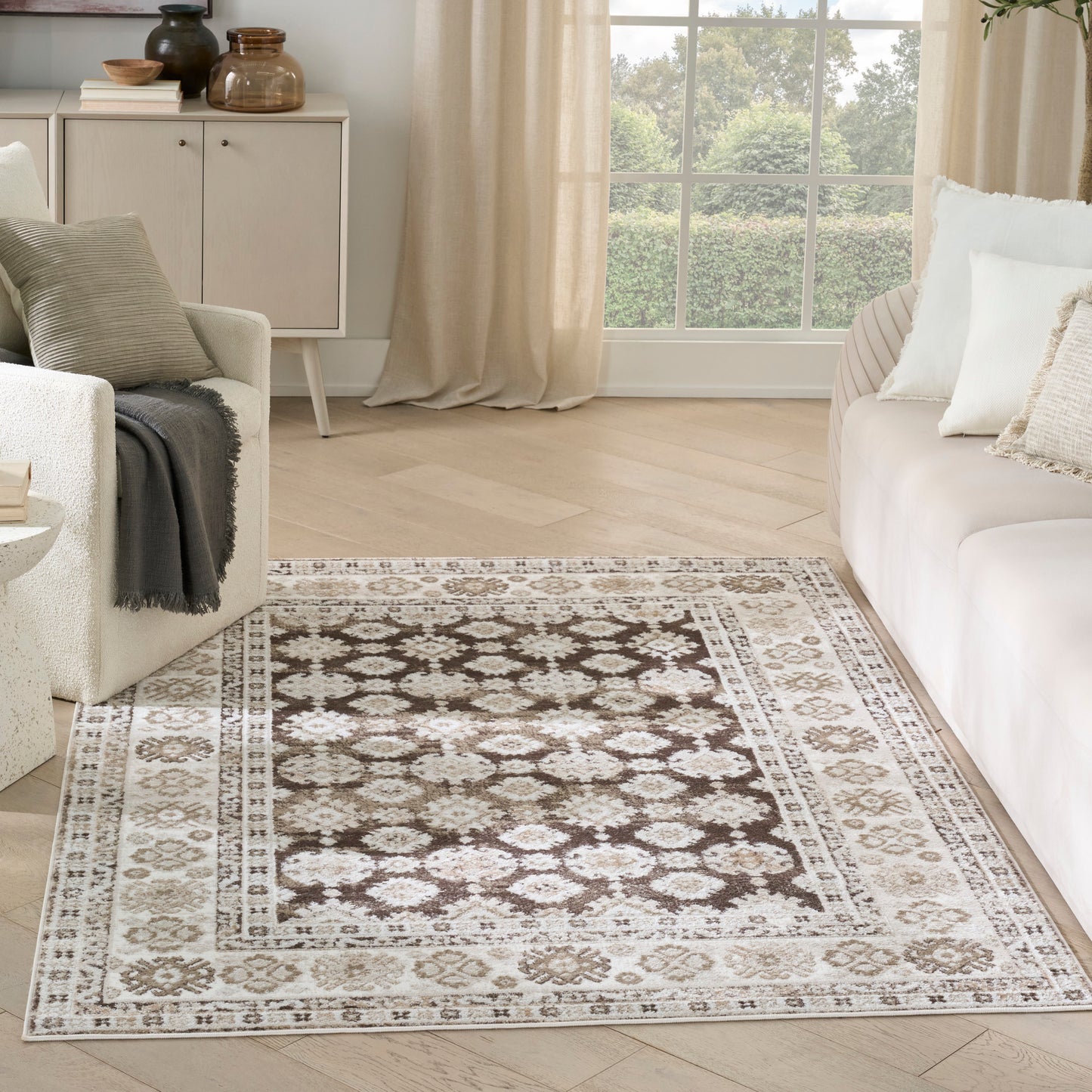 Rectangular cream-brown rug with damask center and floral border in a light, neutral living room.