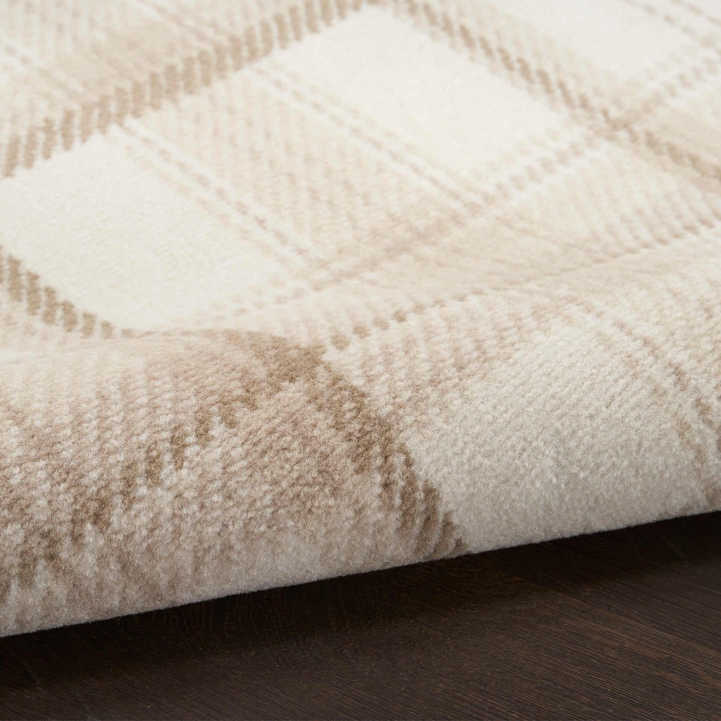 Close-up of plush beige plaid rug with cream and tan checks on dark wood floor.
