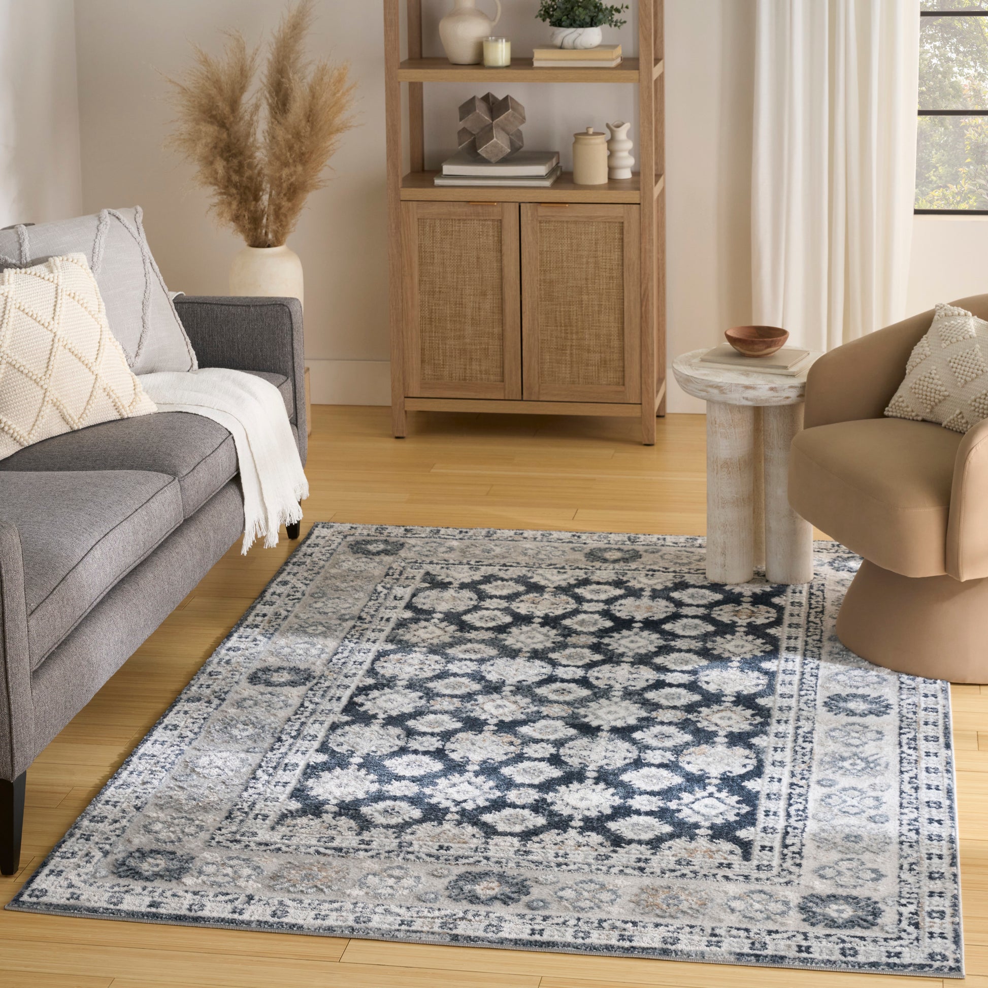 Blue-gray patterned rug in a cozy living room with gray sofa, beige chair & wooden cabinet with woven doors.